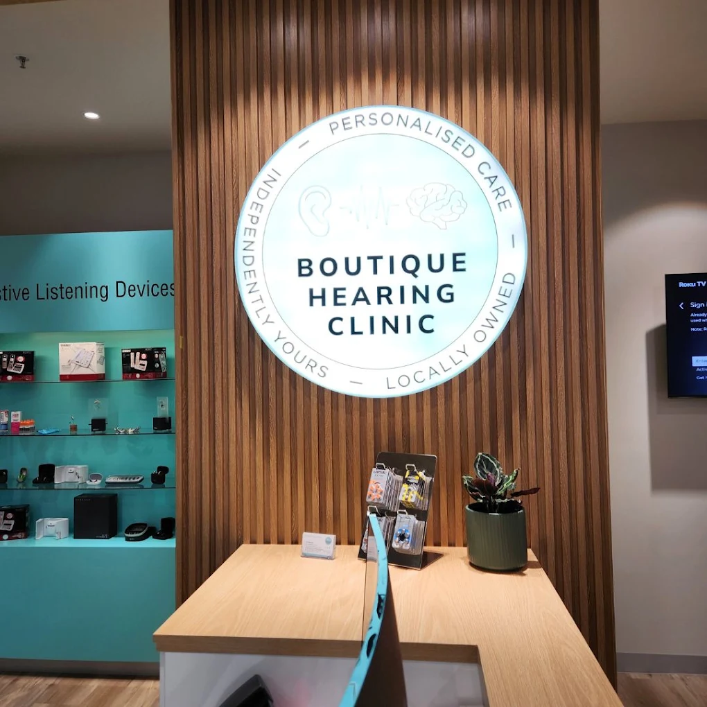 Boutique Hearing Clinic reception with the illuminated logo on warm timber panelling